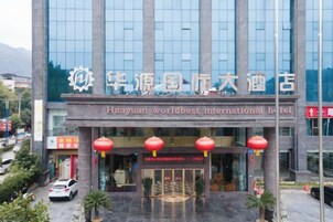 Um hotel com fachada de vidro ampla, entrada destacada com lanternas vermelhas e uma placa indicando ser o Huayuan Worldbest International Hotel.