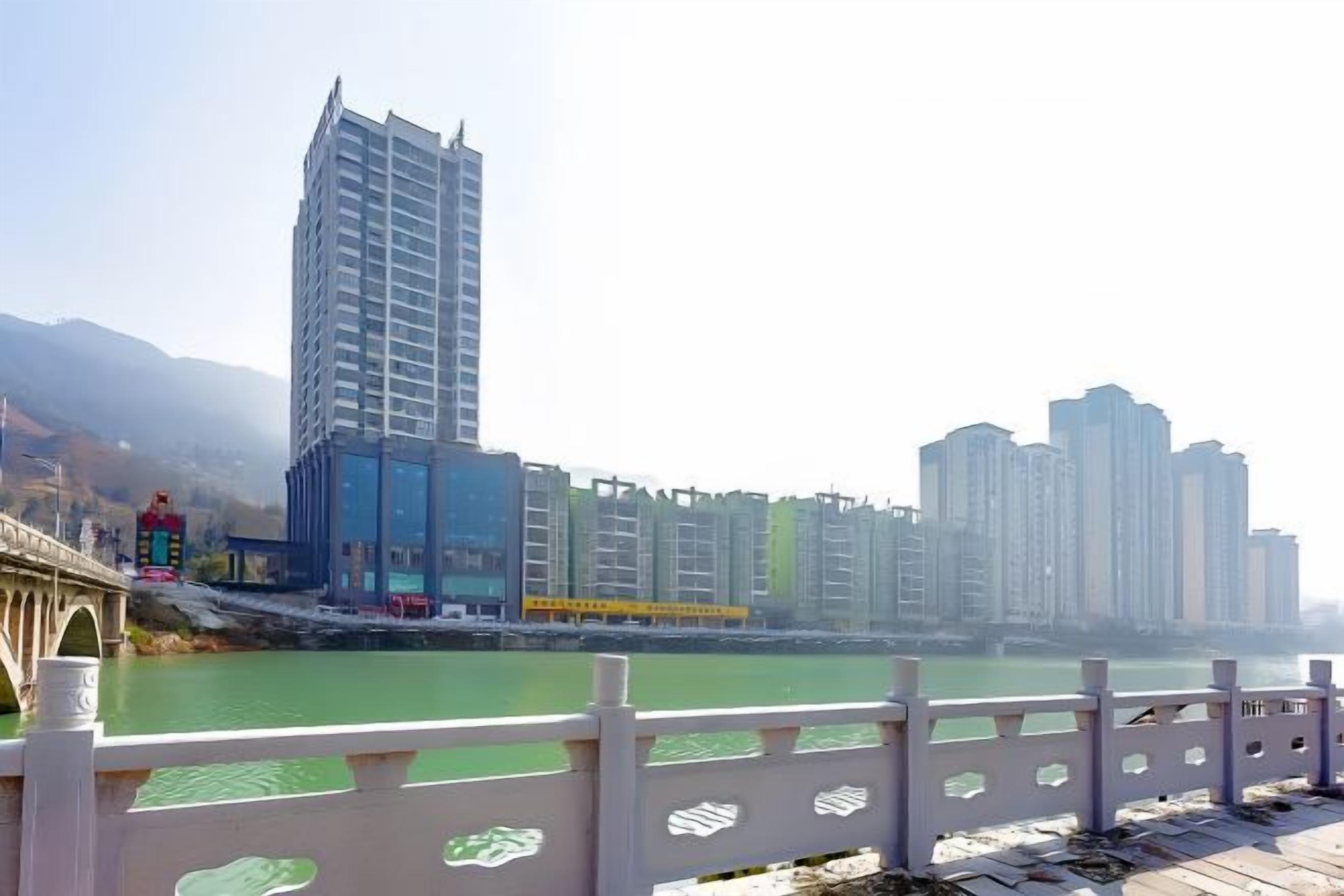 A river with a bridge, modern buildings, and a white railing.