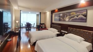 Habitación de hotel con dos camas, zona de comedor y un cuadro grande en la pared.