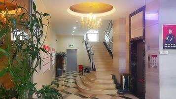 Un'hall di un hotel con una scala, un lampadario e una pianta.