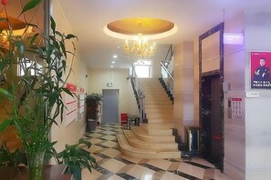 Een hotellobby met een trap, een kroonluchter en een plant.