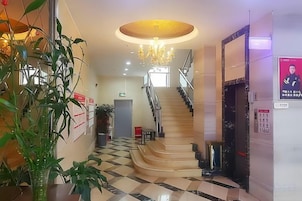 A hotel lobby with a staircase, a chandelier, and a plant.