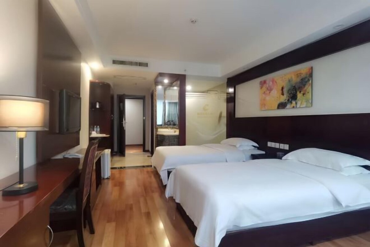 Une chambre d’hôtel avec deux lits, un bureau, une chaise, une télévision et un tableau au mur.