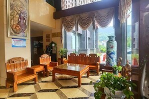 A lobby with wooden furniture, a checkered floor, a large vase, and a painting on the wall. - Huayuan International Hotel (Shiqian)