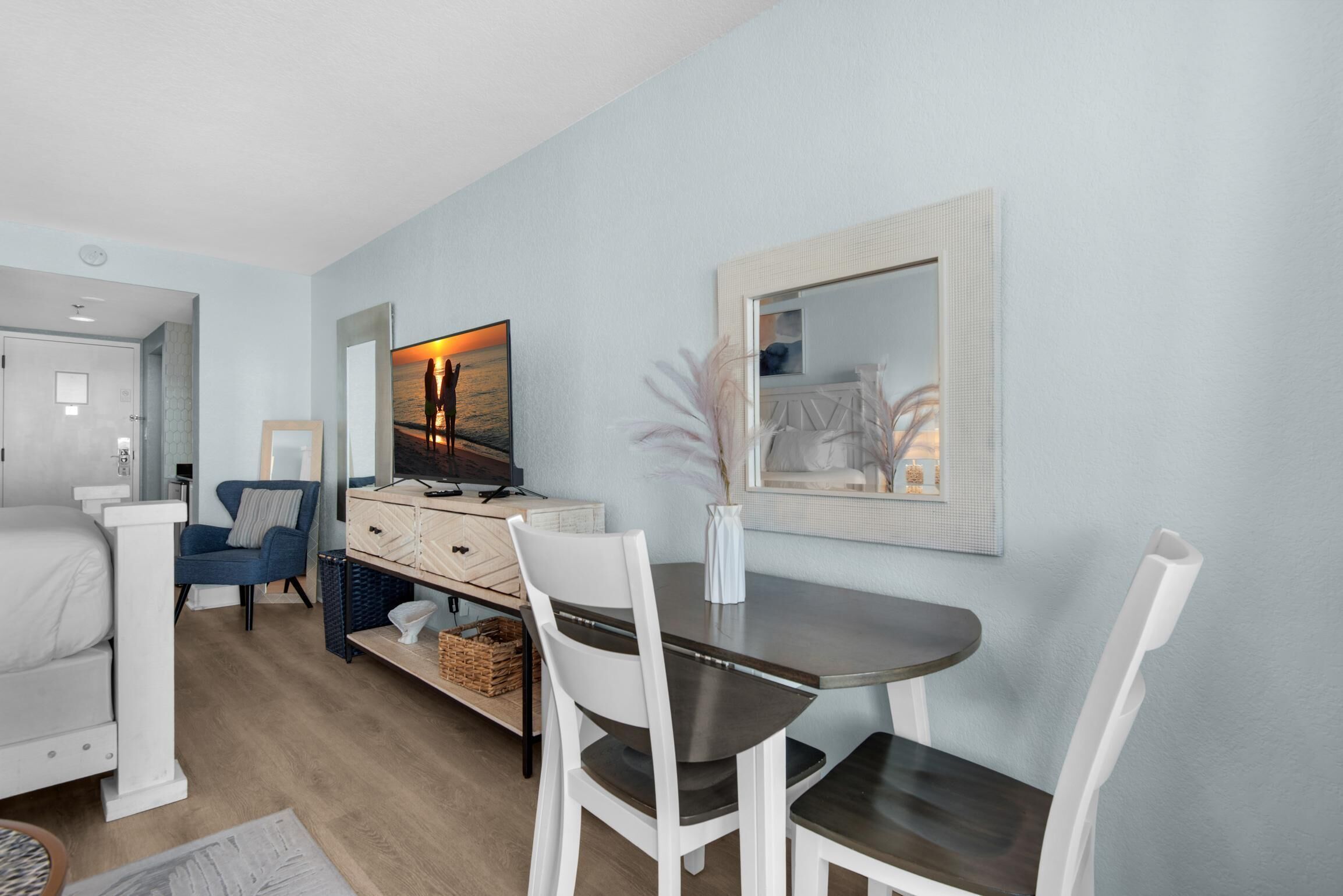 A modern, well-lit room with a dining table, chairs, a sofa, and a TV.