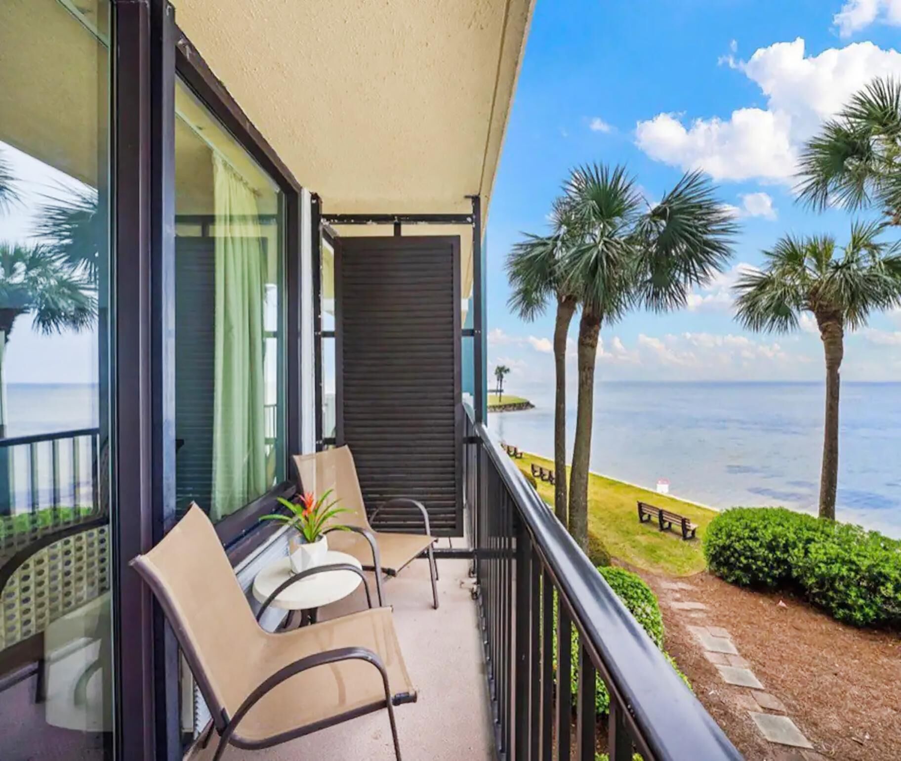A balcony with a table and chairs, a view of the ocean, and palm trees.