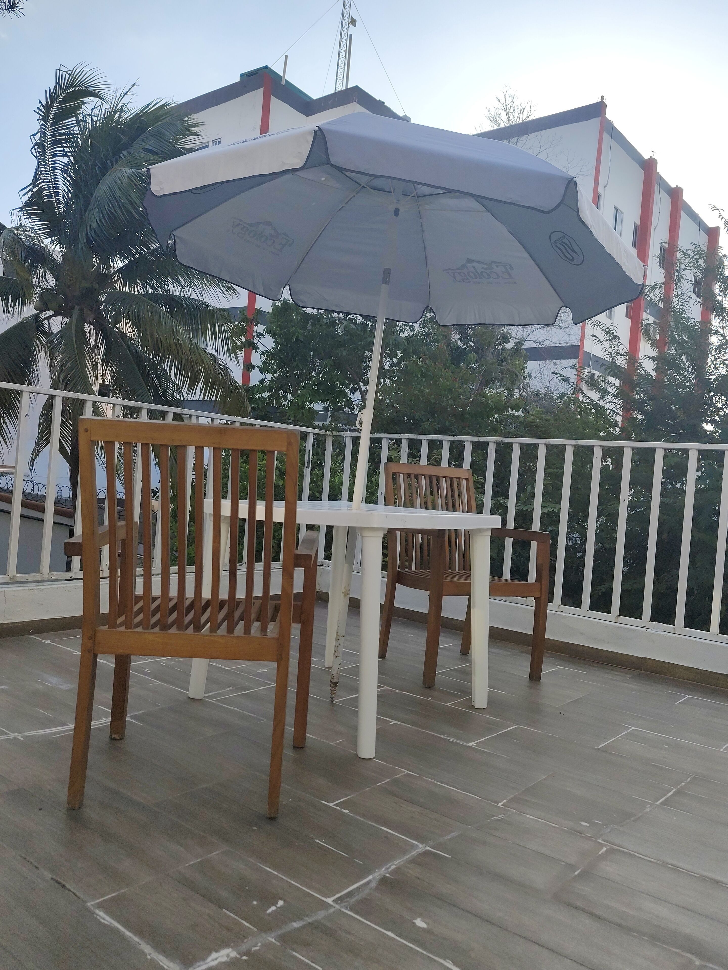 A terrace with wooden chairs and a table under a large umbrella.