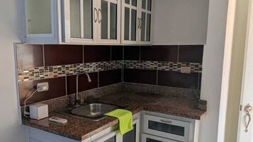A compact kitchen with white cabinets, a granite countertop, and a tiled backsplash.