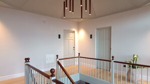 Ein geräumiger Innenraum mit einer Holztreppe, weißen Wänden und einer hängenden Leuchte.