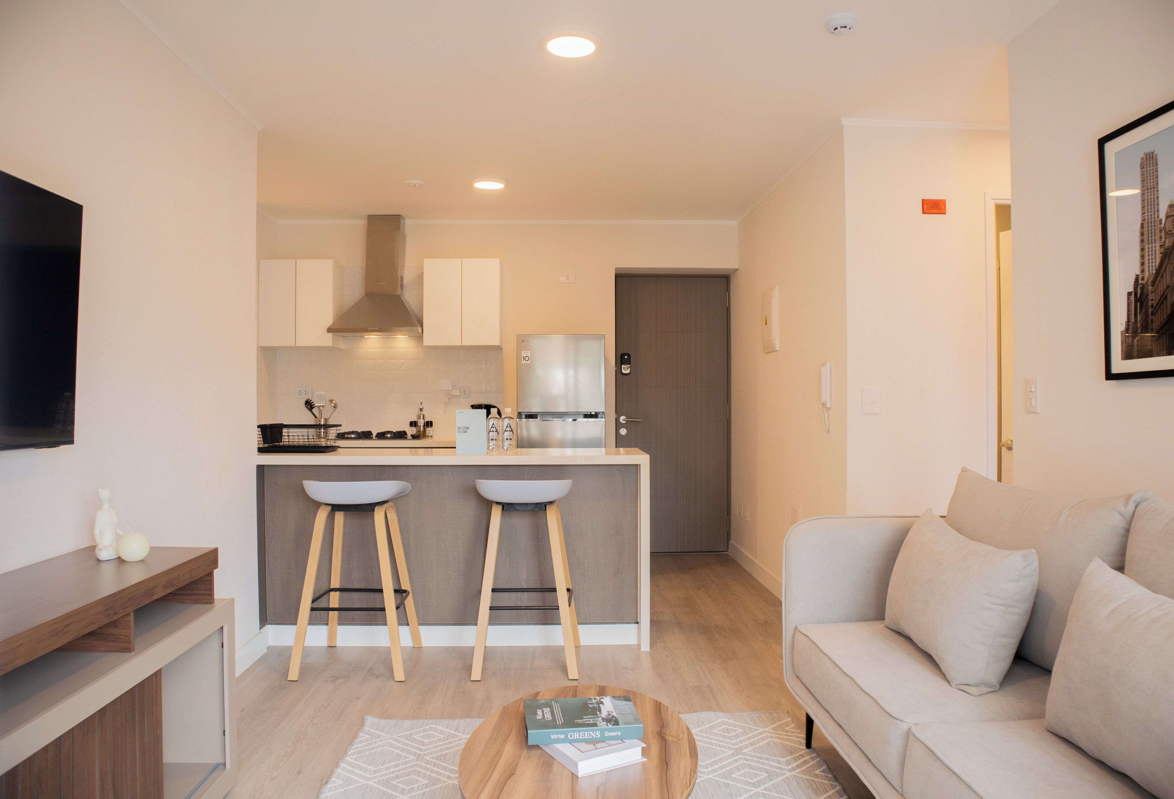 A modern kitchen with white cabinets, a stainless steel refrigerator, and a bar area with stools.
