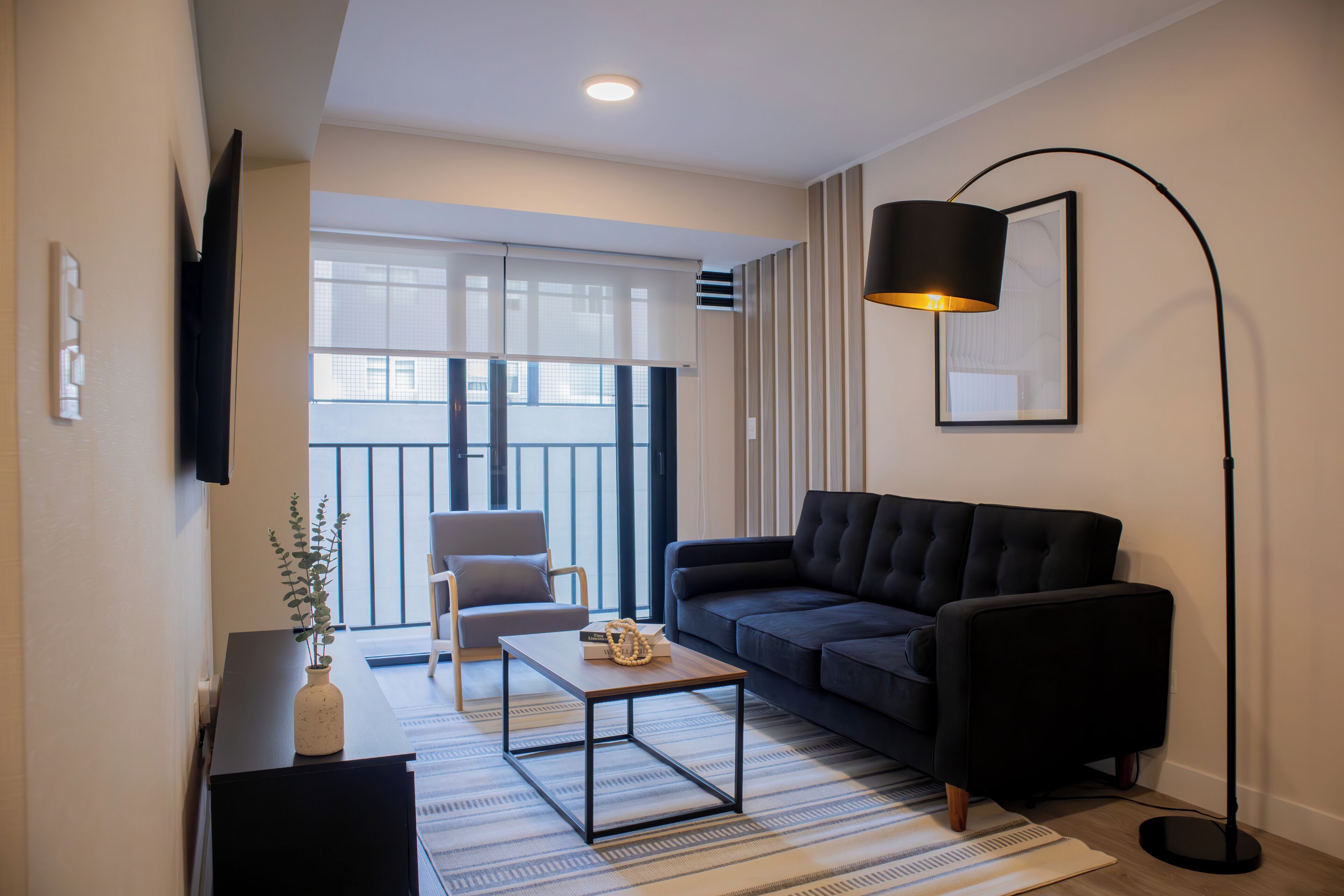 Una sala de estar moderna con un sofá, una mesa de centro, una lámpara de pie y un televisor montado en la pared.