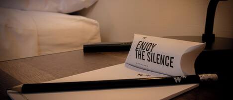Un cuaderno con un lápiz y una tarjeta que dice “ENJOY THE SILENCE” sobre una mesa de madera.