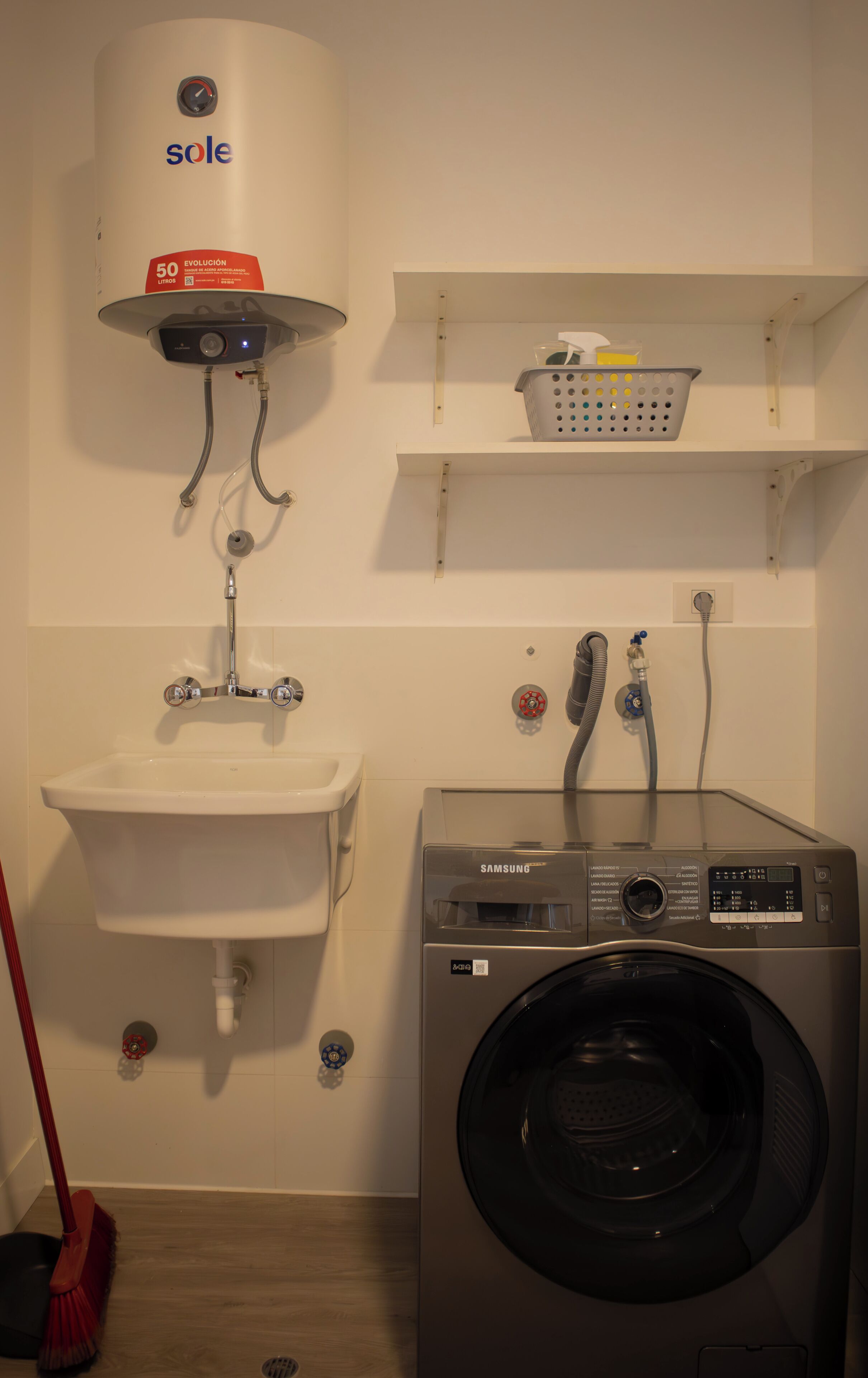 Een wasruimte met een wasmachine, een wasbak en een boiler.