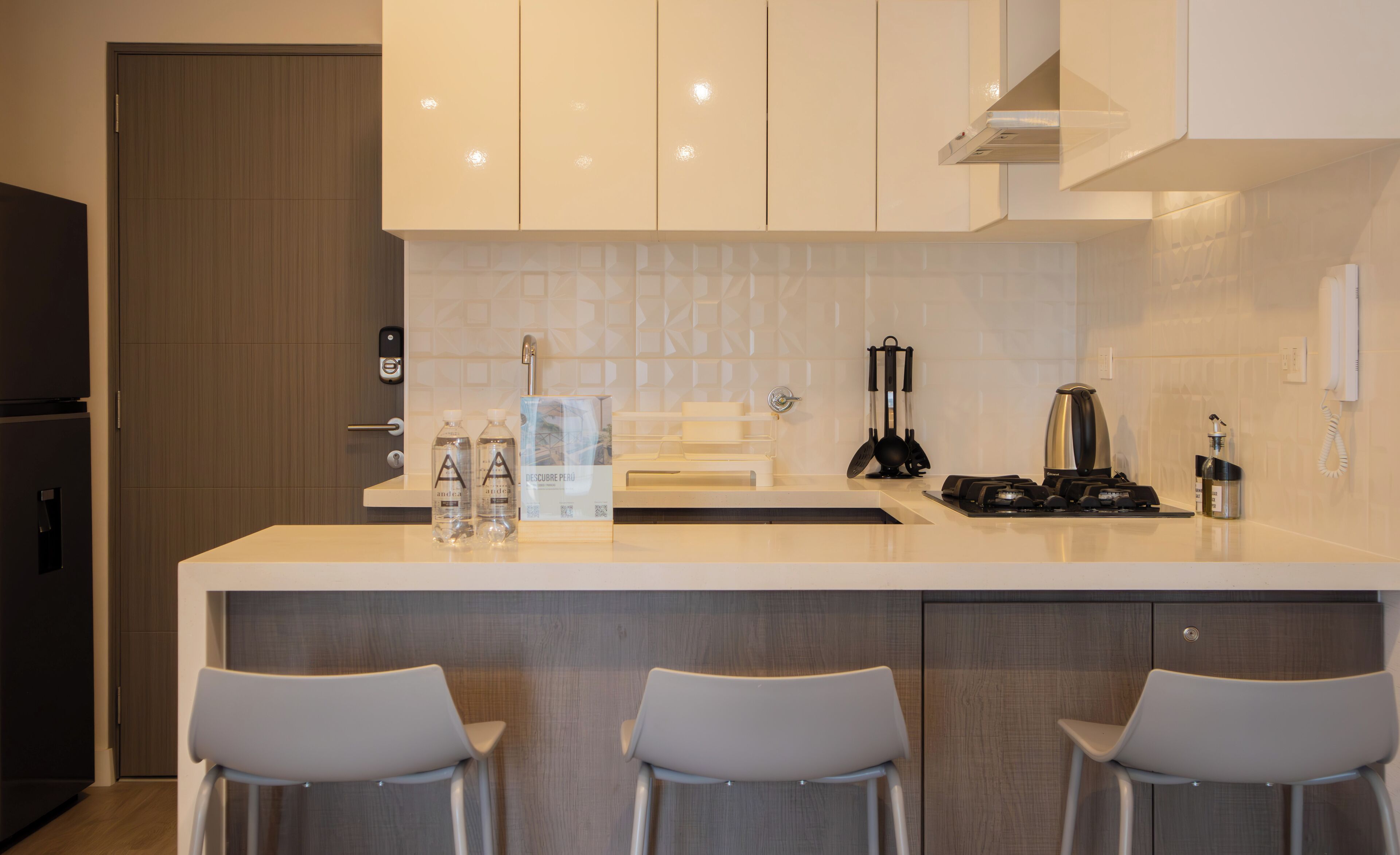Una cocina moderna con una isla central, taburetes de bar, estufa integrada y salpicadero con diseños geométricos.