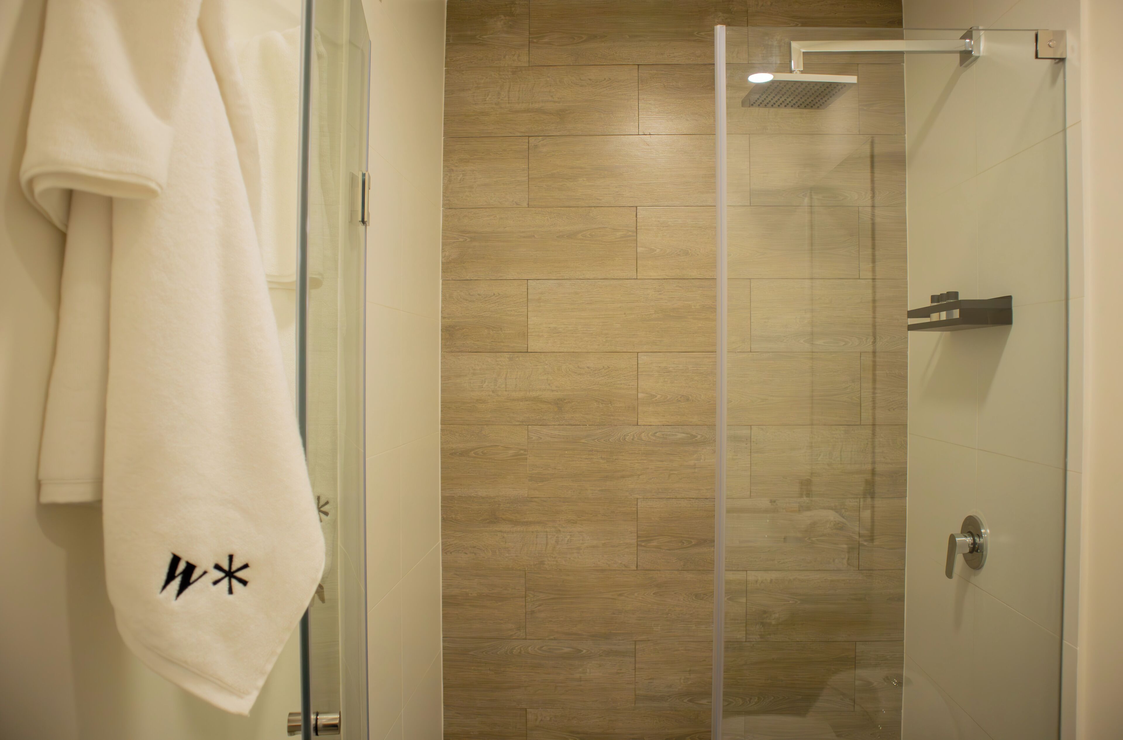 A bathroom with a glass shower enclosure, wooden floor tiles, and a white towel hanging on a rack.