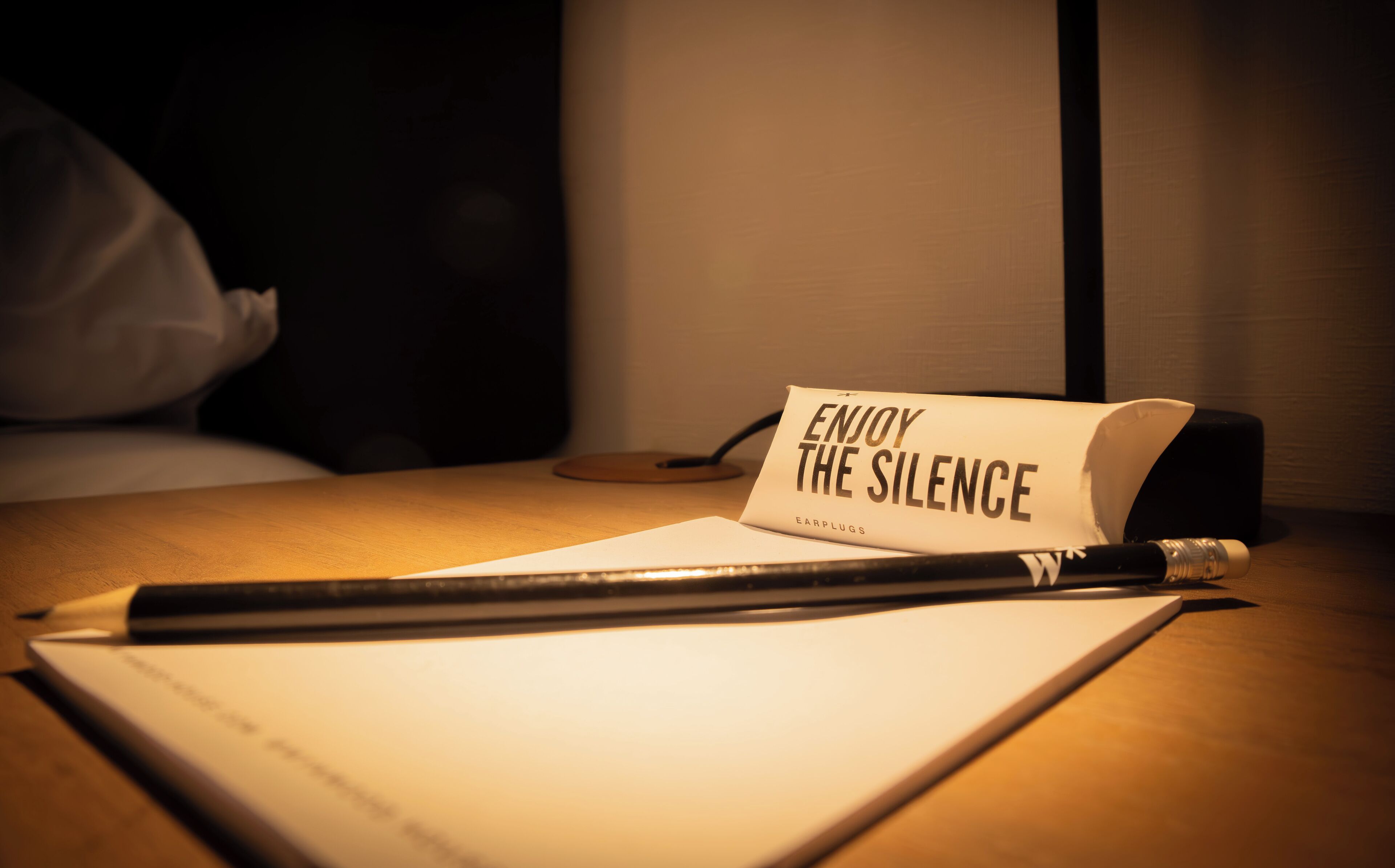 A desk with a notebook, a pen, and a rolled-up sign that reads "ENJOY THE SILENCE" with the brand "EARPLUGS" visible.