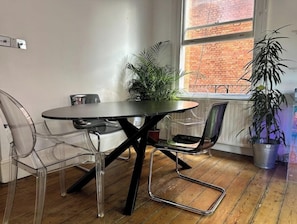 Uma área de jantar com uma mesa redonda, cadeiras transparentes e plantas em vasos.