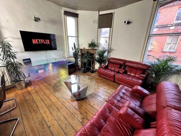 Uma sala de estar moderna com um sofá de couro vermelho, uma mesa de centro de vidro e uma televisão de tela plana fixada na parede.