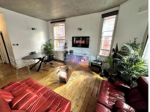 Uma sala de estar moderna com um sofá de couro vermelho, uma mesa de centro de vidro e uma TV fixada na parede.