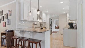 Una cocina moderna con armarios blancos, encimera de granito y dos taburetes de bar.