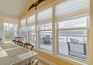 A dining area with a large table and chairs, large windows with blinds, and a view of outdoor seating. - Sunkissed Shores-Rare Flat Lot w/Beautiful Views, Dock, Hot Tub (Winchester)
