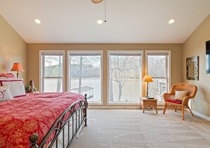 A bedroom with a large bed, a chair, a small table, and a view of a body of water through large windows. - Sunkissed Shores-Rare Flat Lot w/Beautiful Views, Dock, Hot Tub (Winchester)
