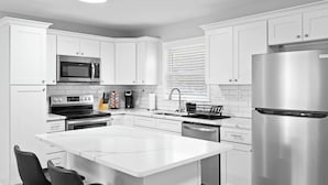 Cocina moderna con armarios blancos, electrodomésticos de acero inoxidable y una isla central con asientos.