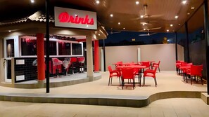 Relax in our outdoor seating area, where you can enjoy a drink at the counter or sit at a table with a red chair.