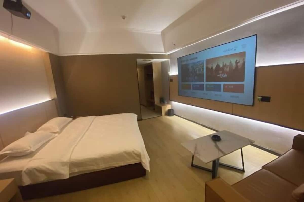 A hotel room with a bed, a small table, a TV mounted on the wall, and a mirror.