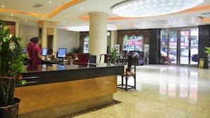 A hotel reception area with a reception desk, a large chandelier, and a glass door entrance.