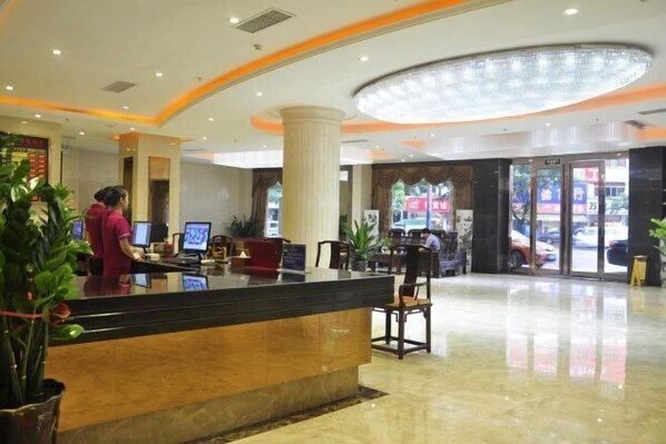 A hotel reception area with a reception desk, a large chandelier, and a glass door entrance.