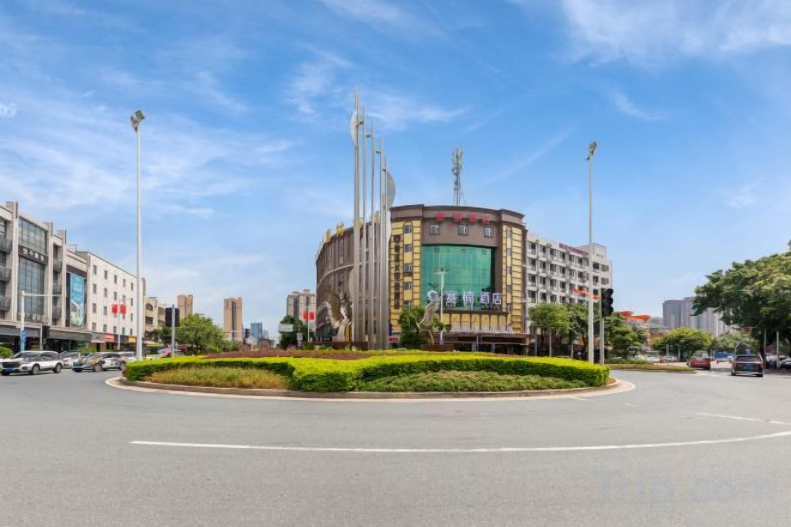 Una glorieta con un área verde central, rodeada de edificios con señalización comercial.