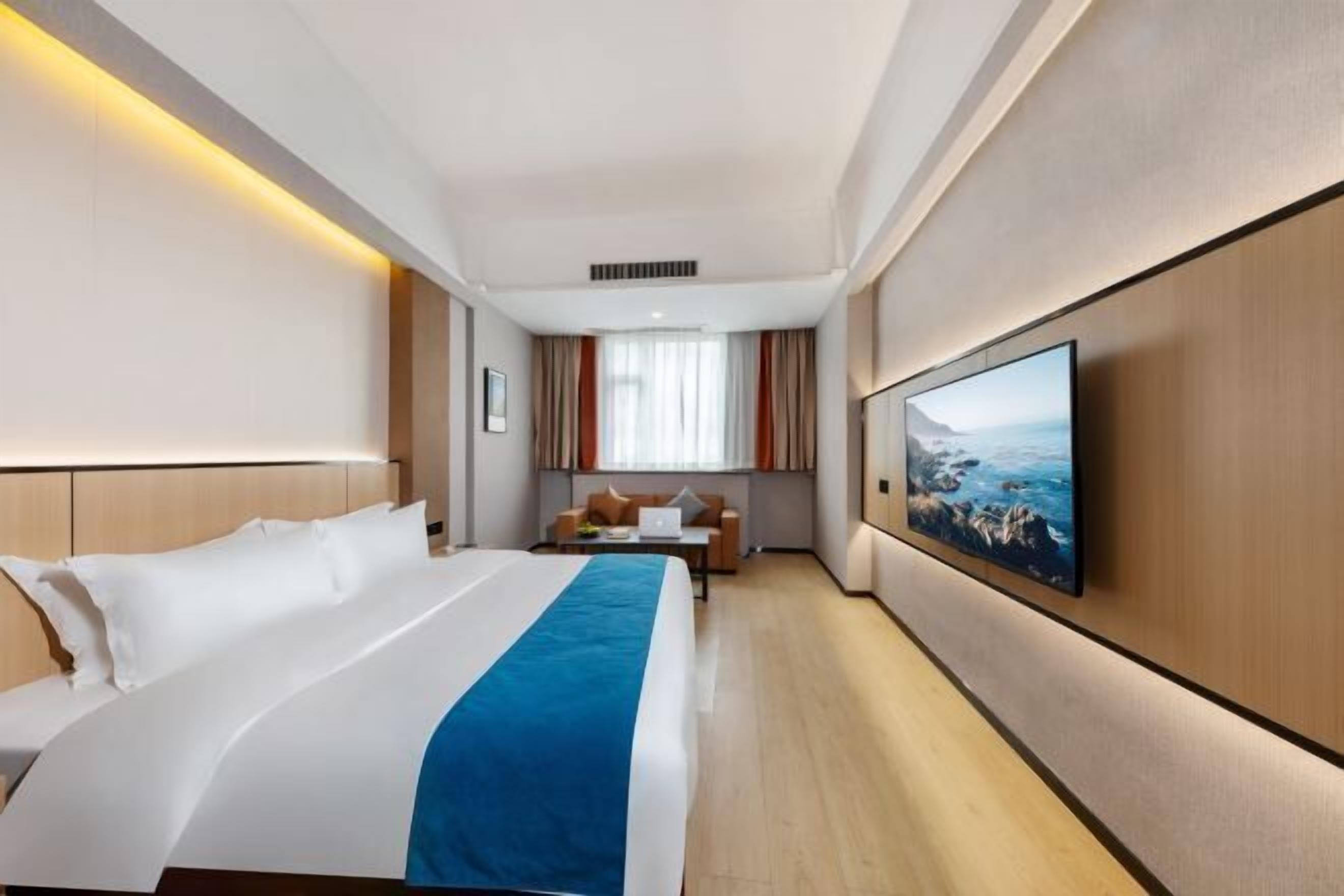 Habitació d'hotel amb un llit gran, un escriptori, una cadira, un televisor de pantalla plana fixat a la paret i una finestra amb cortines.