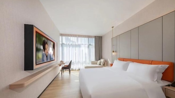 A hotel room with a large bed, a desk, a chair, and a window with curtains.