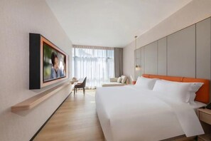 A hotel room with a large bed, a desk, a chair, and a window with curtains.