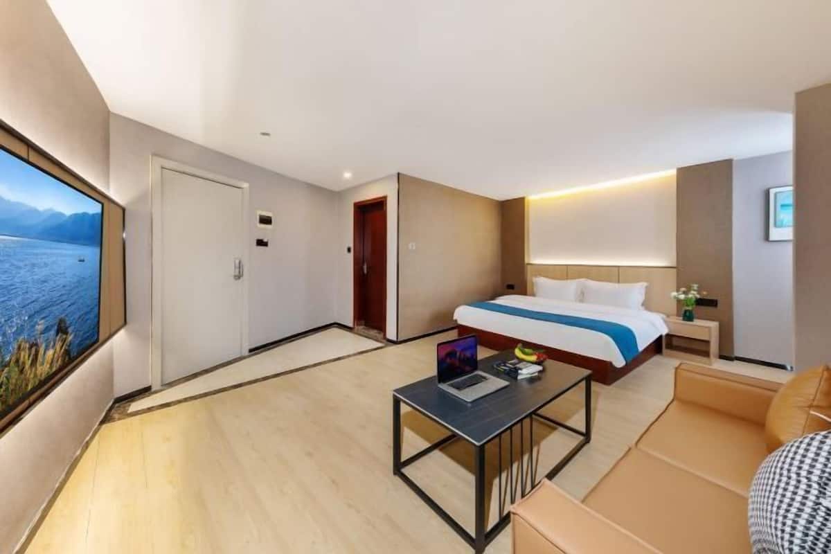 A modern hotel room with a bed, a desk, a sofa, and a large TV screen.