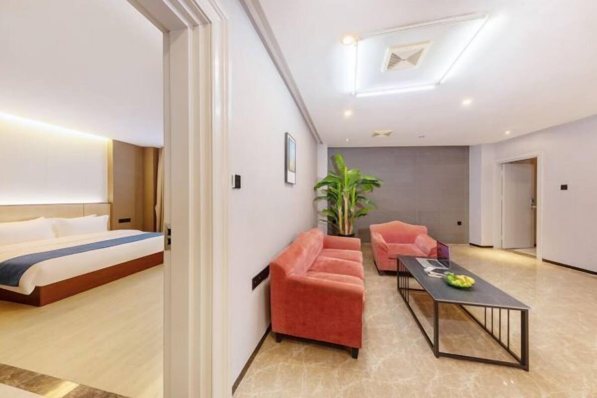 A modern hotel room with a bed, a seating area with a table, and a potted plant.