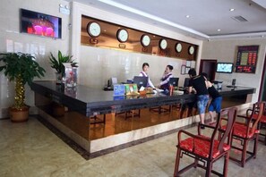 A hotel reception area with a counter, two receptionists, a TV screen, and a clock. - Saiyan Hotel (Zhongshan Bus Terminal) (Zhongshan)
