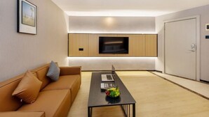 A modern living room with a sofa, a coffee table with a laptop and fruit, a flat-screen TV, and a door.