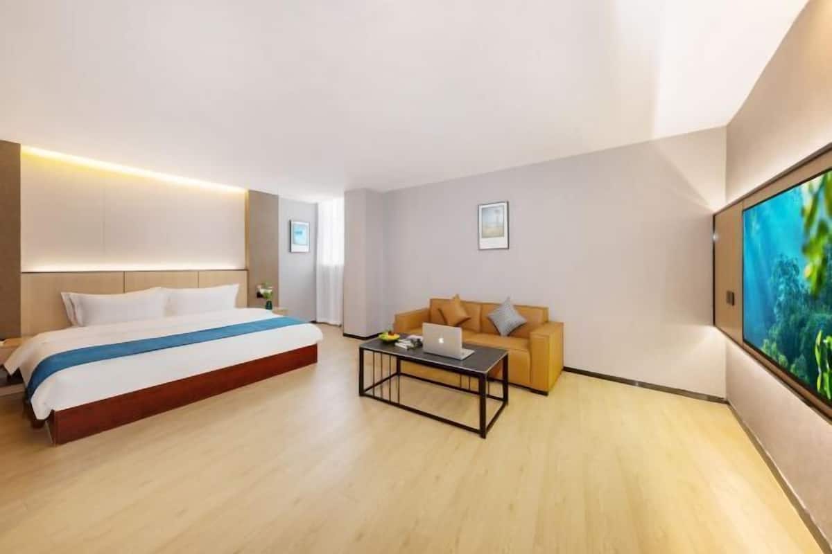 A hotel room with a bed, a sofa, a coffee table, and a large TV screen.