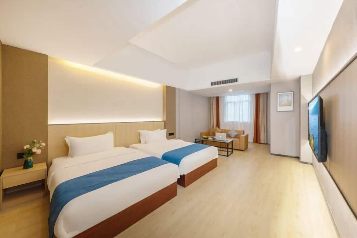 A hotel room with two beds, a desk, a chair, a flat-screen TV, and a window.