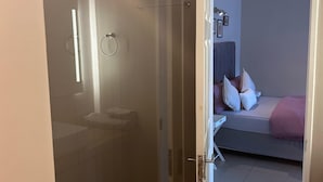 Et værelse med brusekabine i glas, en seng med puder og et natbord.