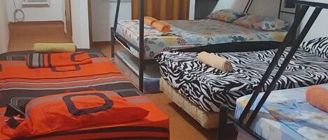 A dormitory room with bunk beds, a window with bars, a radiator, and a wooden ceiling.