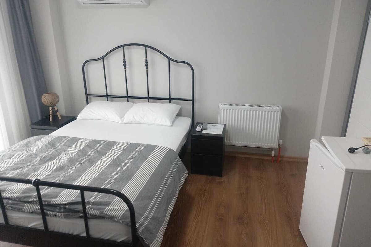 A bedroom with a bed, bedside table, nightstand, radiator, and a small white cabinet.