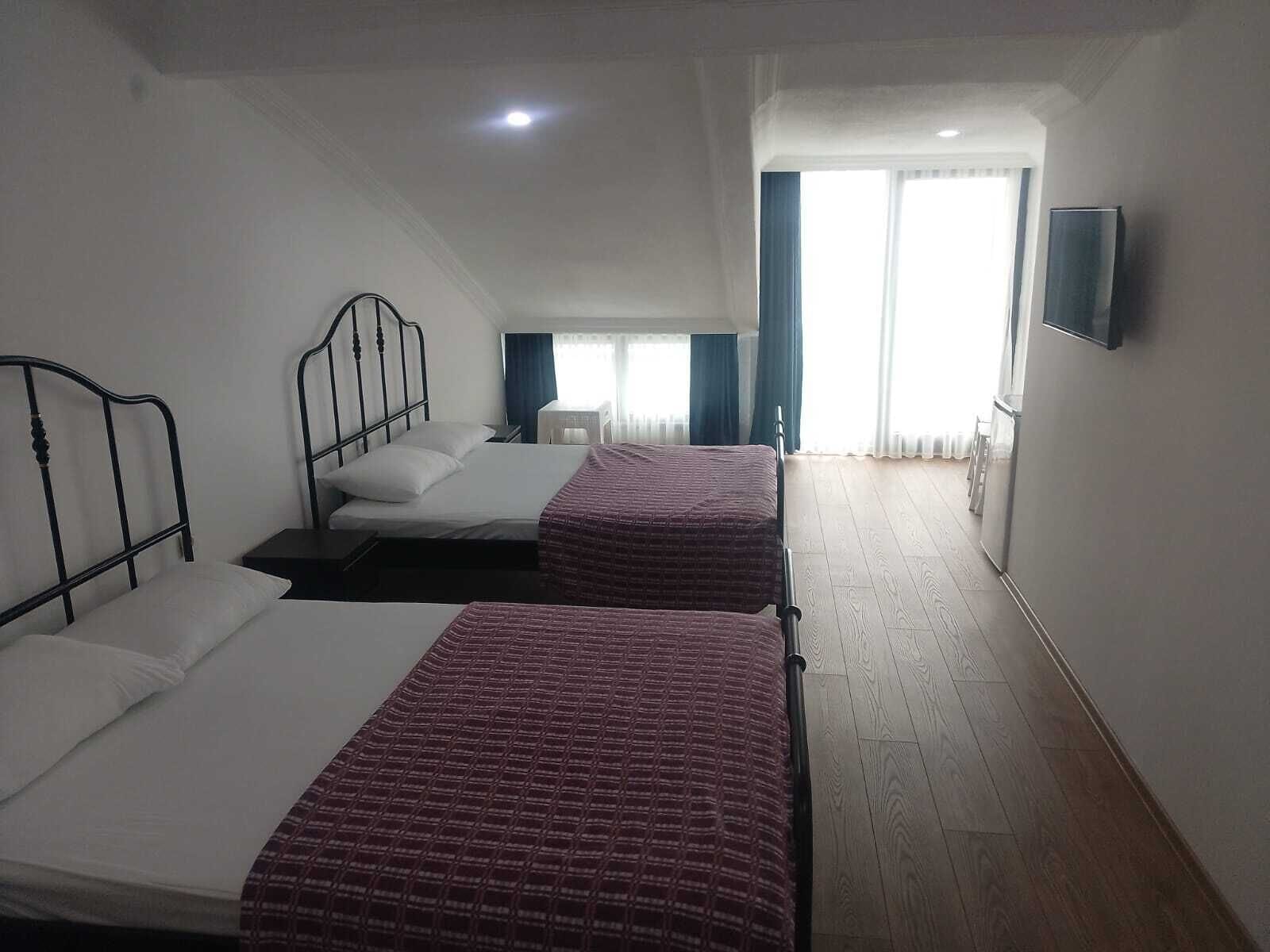 A hotel room with two beds, a TV mounted on the wall, and a window with curtains.