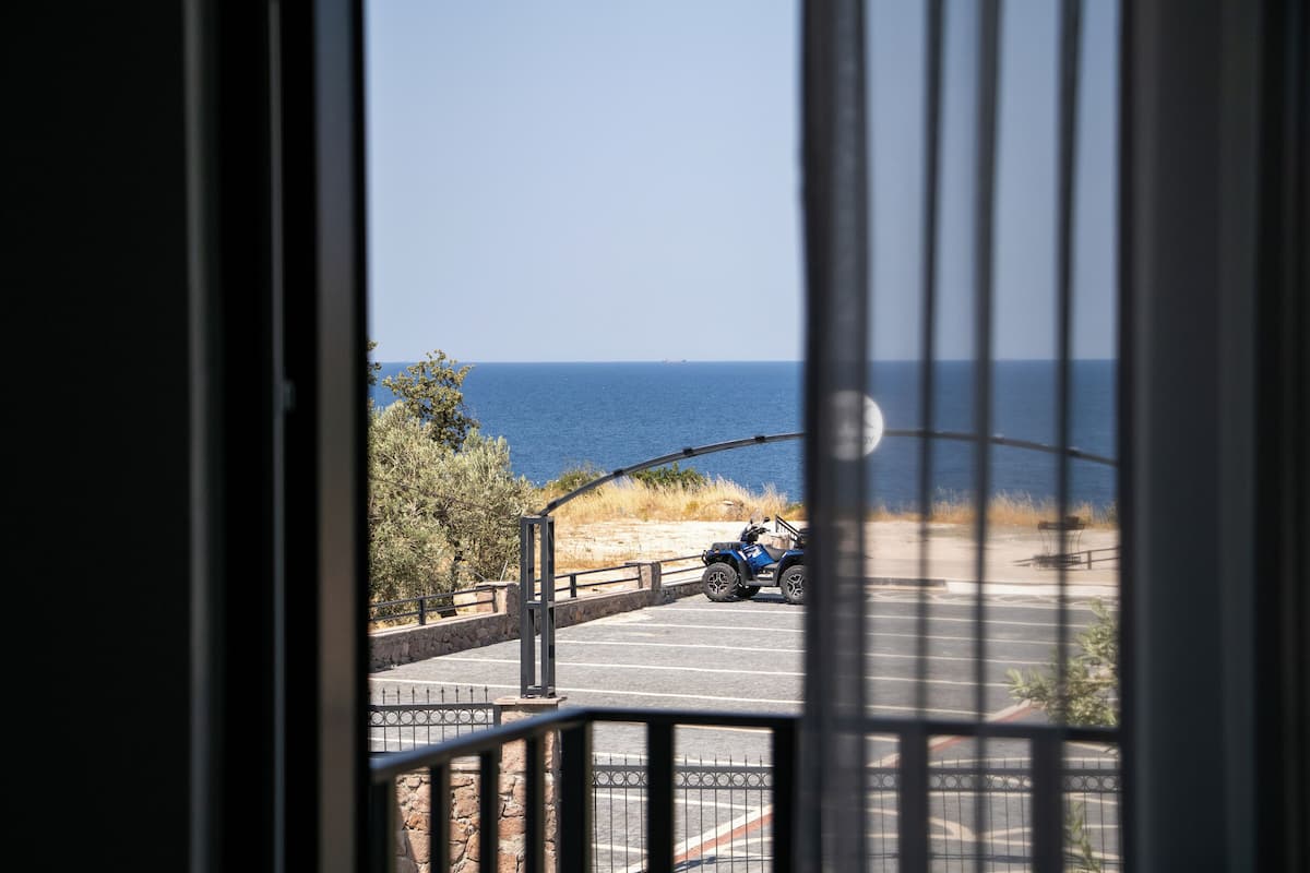 A view through a window of a parking area with a blue vehicle, a stone wall, and a clear blue sky.