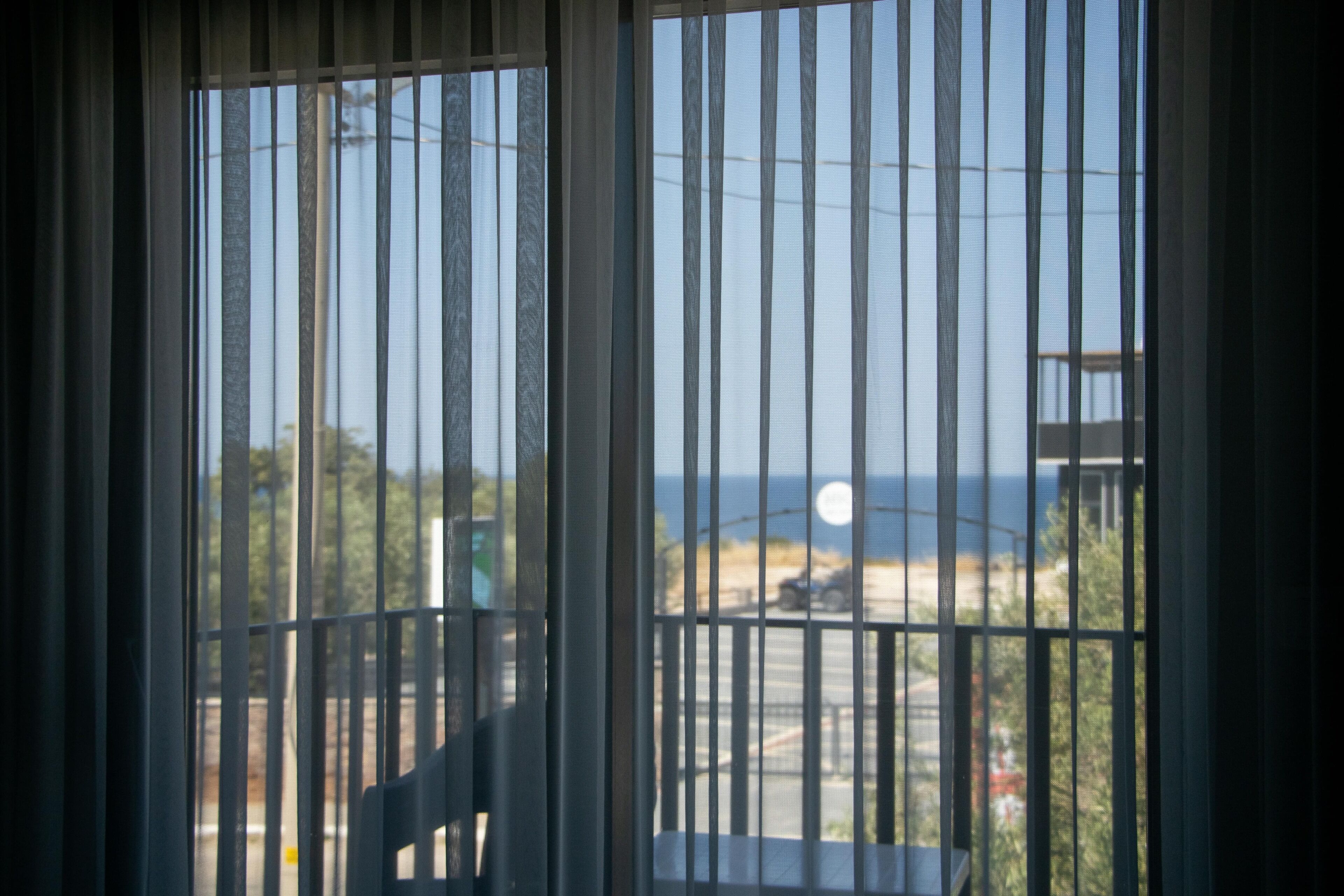 A window with vertical bars, a chair, and a view of the sea and a building.