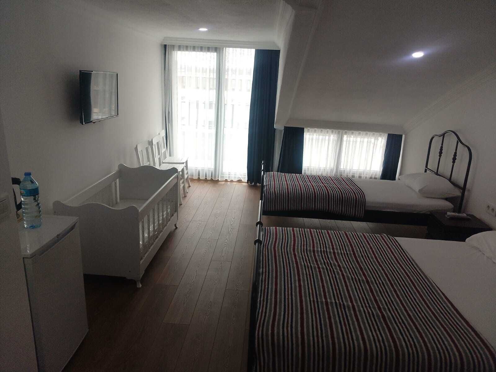 Habitación de hotel con cama, escritorio, silla, televisor y ventana con cortinas.