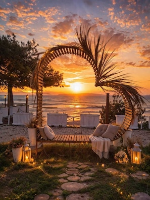 Een strandsetting met een houten boog, lounge fauteuils en lantaarns.