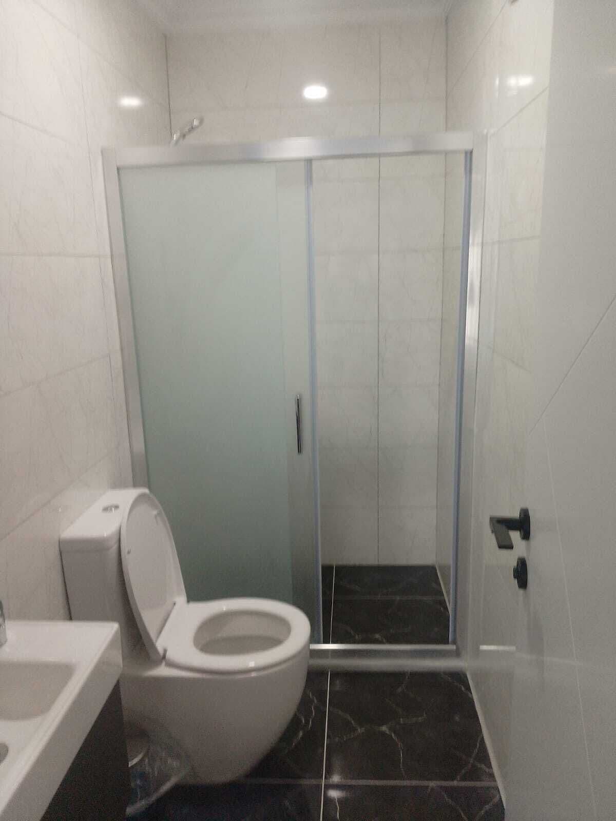 Un baño con inodoro, cabina de ducha y lavamanos.